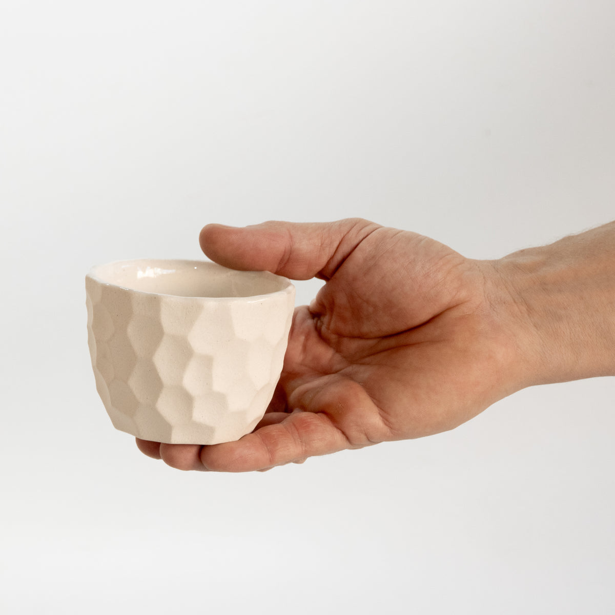 A hand holding a small, textured ceramic cup against a plain white background.